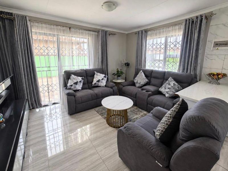 A bright and well-maintained living room featuring polished tiled flooring, large windows with curtains, and sliding glass doors leading to the exterior.