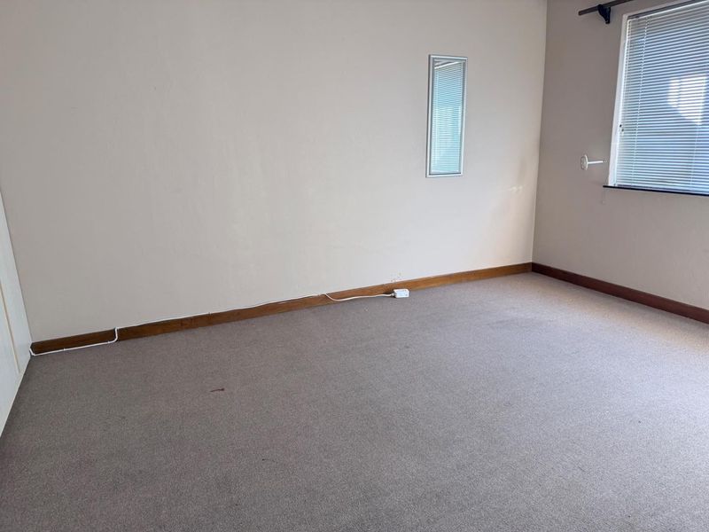 An empty bedroom featuring neutral wall tones, carpeted flooring, timber skirting boards, and a window fitted with venetian blinds.