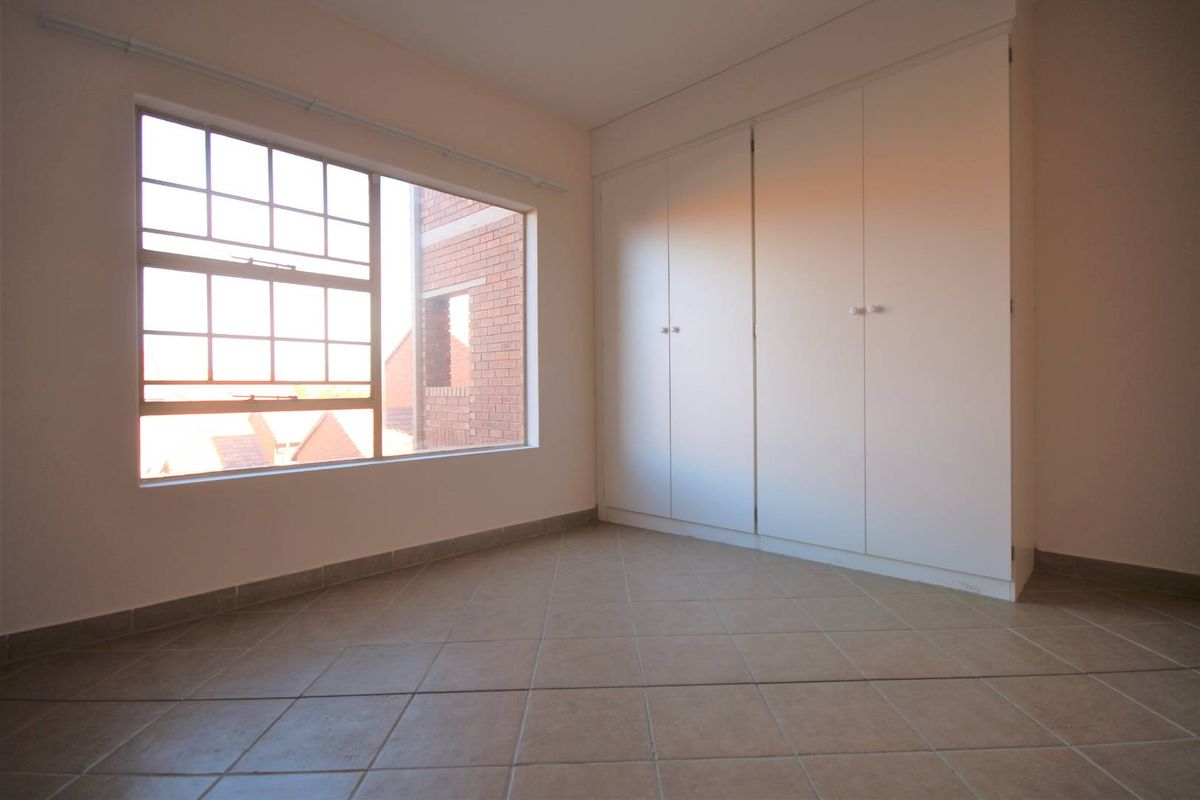A bright, empty bedroom featuring neutral tiled flooring and ample built-in cupboard storage, offering a clean canvas for personalization.