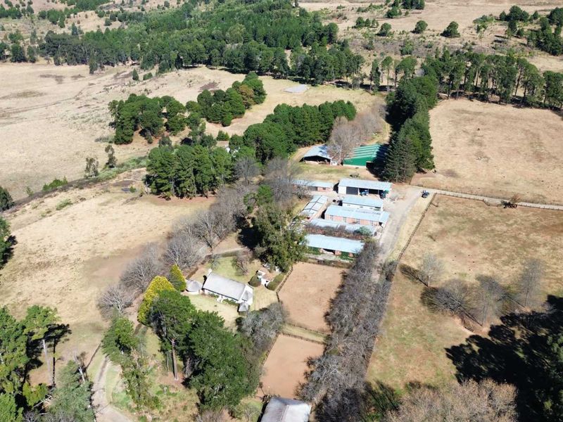 Aerial view of a large farm property featuring multiple outbuildings, fenced paddocks, and extensive surrounding landscape.