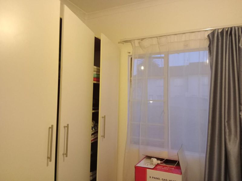 A bedroom featuring a white built-in wardrobe with modern handles and a window with installed curtain rails.