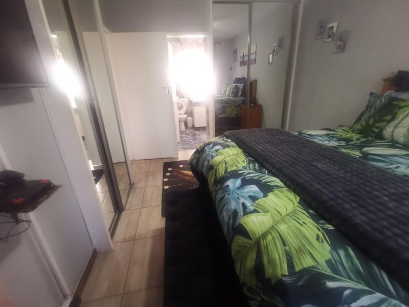 Bedroom featuring tiled flooring and built-in mirrored sliding wardrobes, with direct access to an en-suite bathroom.