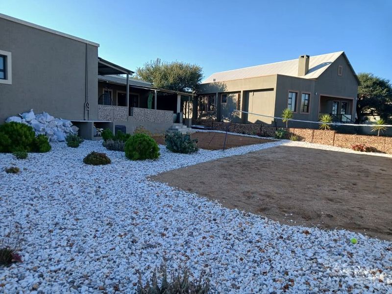 Spacious rear exterior view featuring a covered patio, stone retaining walls, and low-maintenance gravel landscaping between two residential structures.