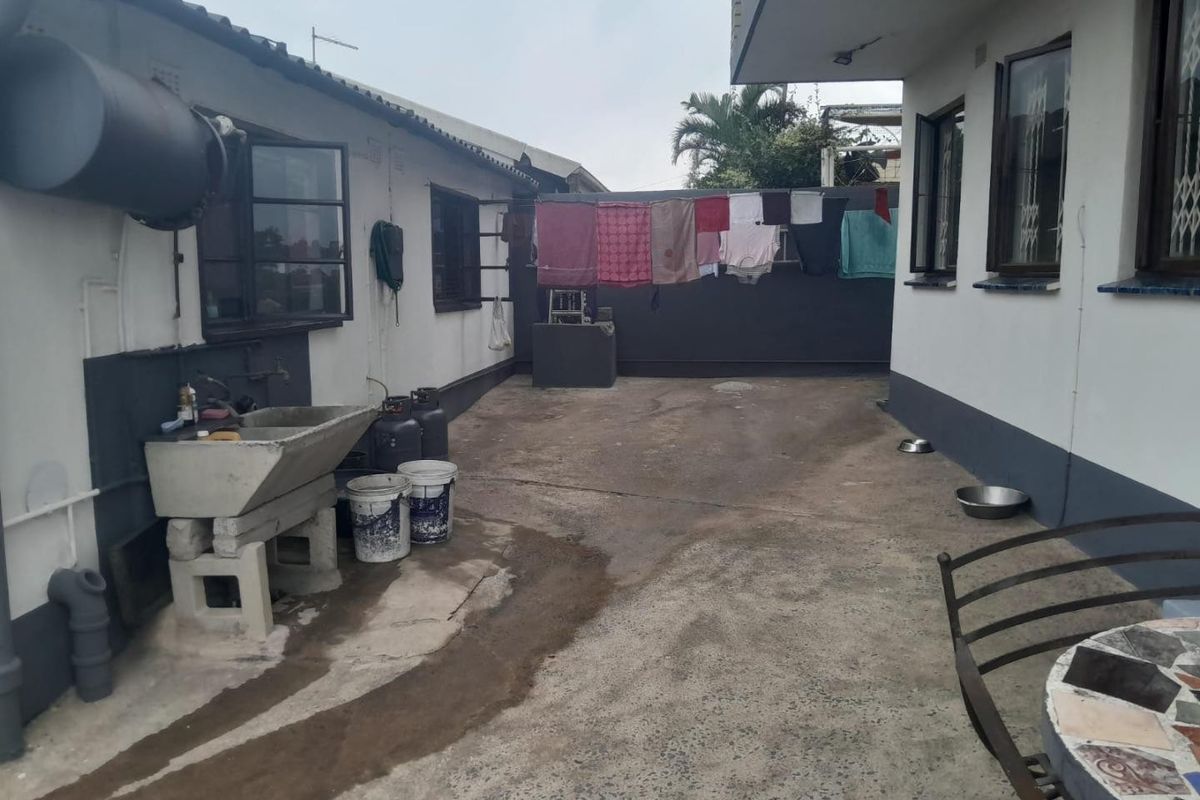 A functional rear courtyard area featuring a concrete wash basin, security-barred windows, and paved flooring, providing practical outdoor utility space.