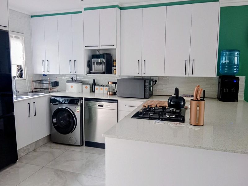 Modern kitchen featuring white cabinetry, stone countertops, a gas hob, and integrated appliances with tiled flooring and a tiled backsplash.