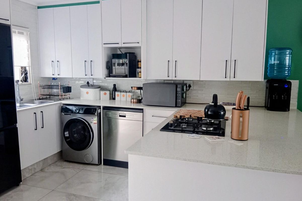 Modern kitchen featuring white cabinetry, stone countertops, a gas hob, and integrated appliances with tiled flooring and a tiled backsplash.