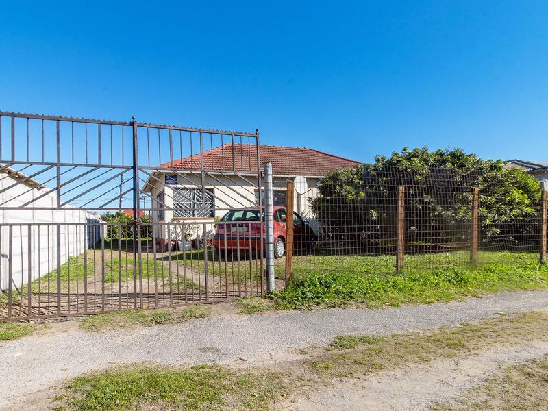 Front exterior view of a single-story house featuring a metal driveway gate, wire mesh fencing, and a tiled roof.