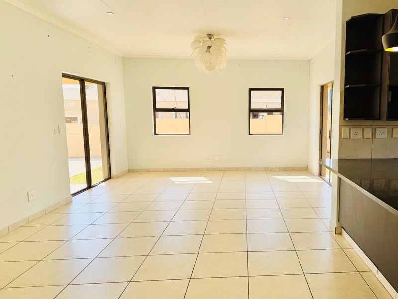 Spacious open-plan living and kitchen area featuring neutral tiled flooring, abundant natural light, and direct access to the outdoor space through sliding doors.