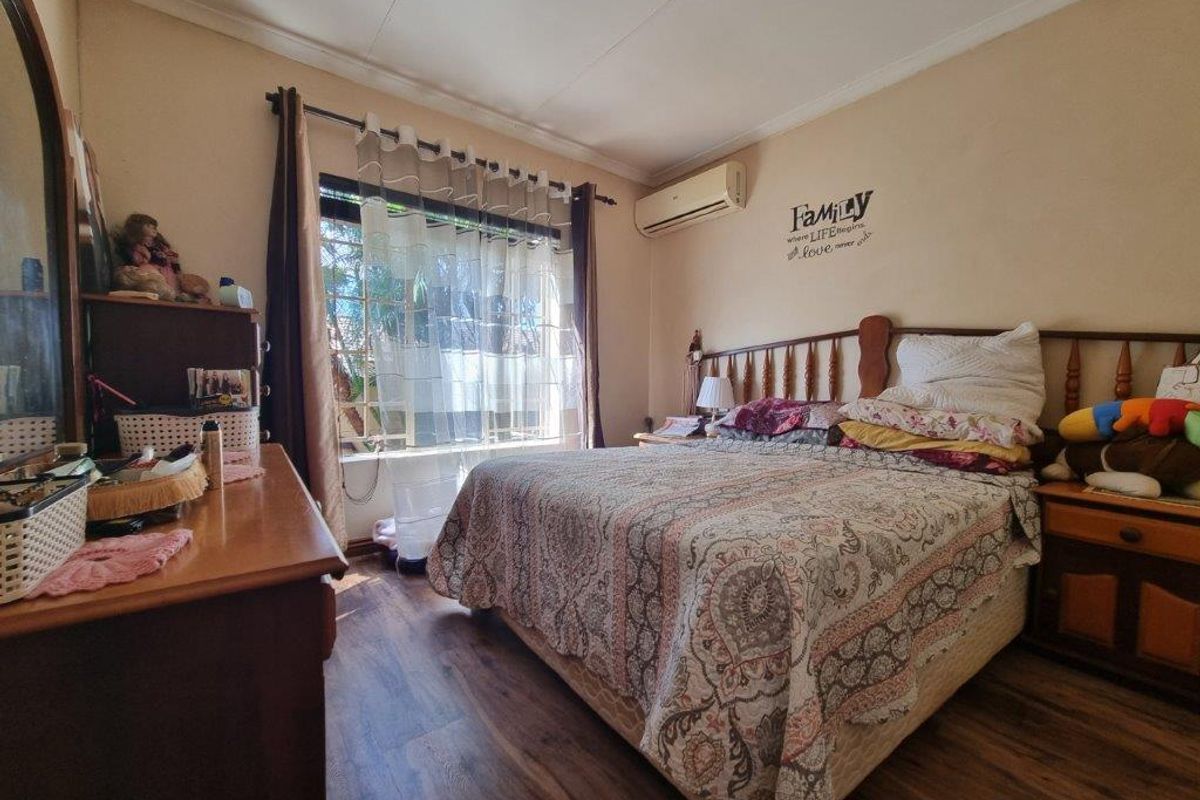 A functional bedroom featuring laminate flooring, a wall-mounted air conditioning unit, and a window fitted with security bars.