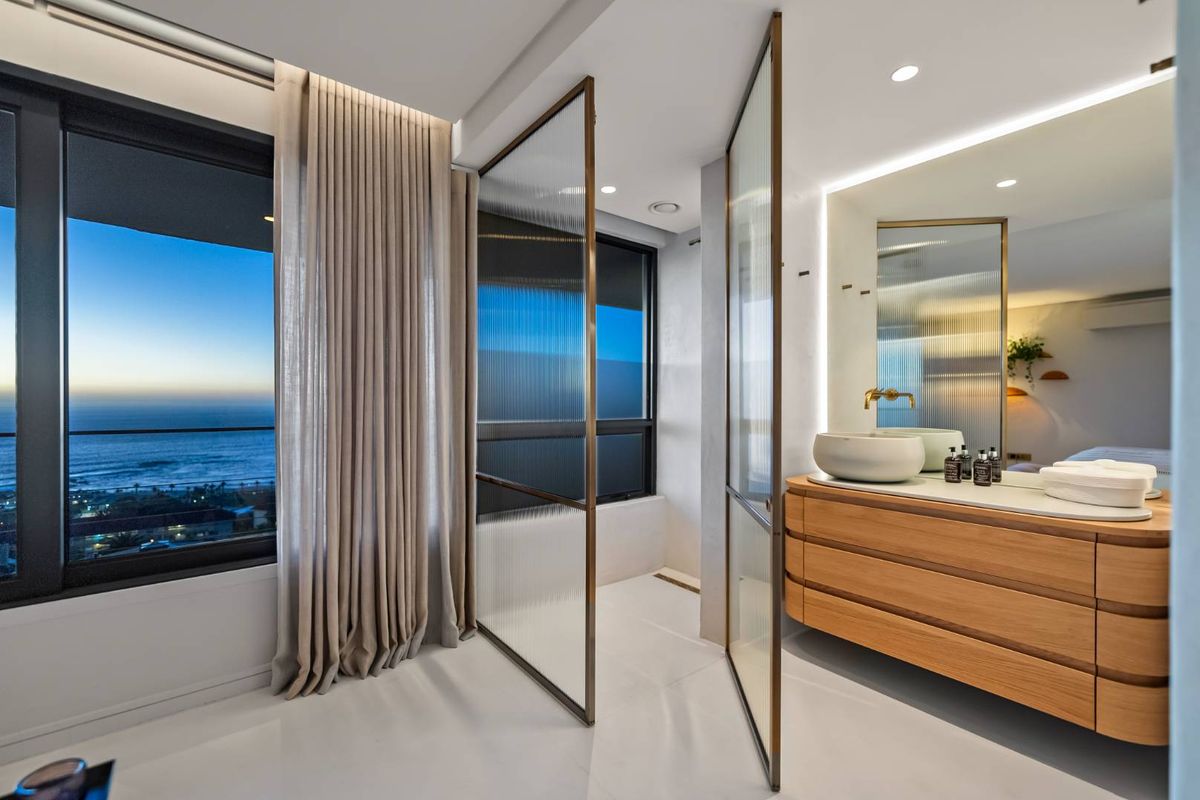 Modern luxury bathroom featuring a floating timber vanity, vessel sink, brass fixtures, and a fluted glass shower screen with stunning ocean views.