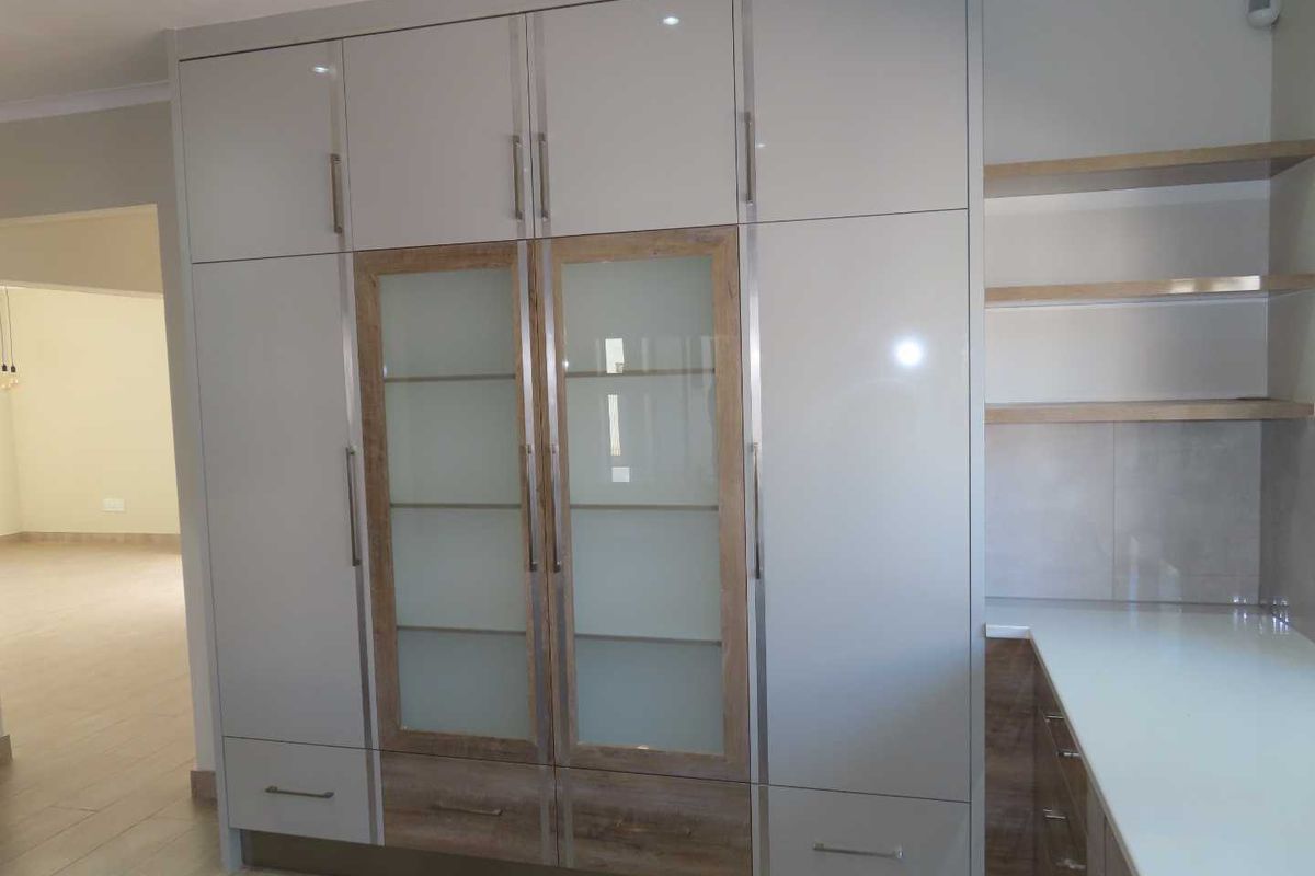 Modern kitchen cabinetry featuring high-gloss grey doors, glass-fronted display cabinets, integrated shelving, and sleek stone countertops.