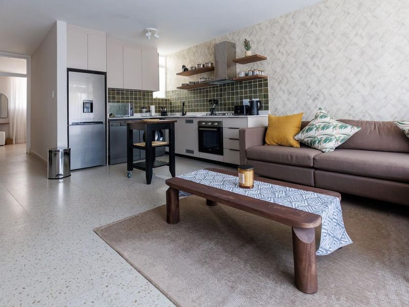 Modern open-plan living area featuring a well-appointed kitchen with built-in cabinetry, tiled backsplash, and sleek terrazzo flooring throughout the space.