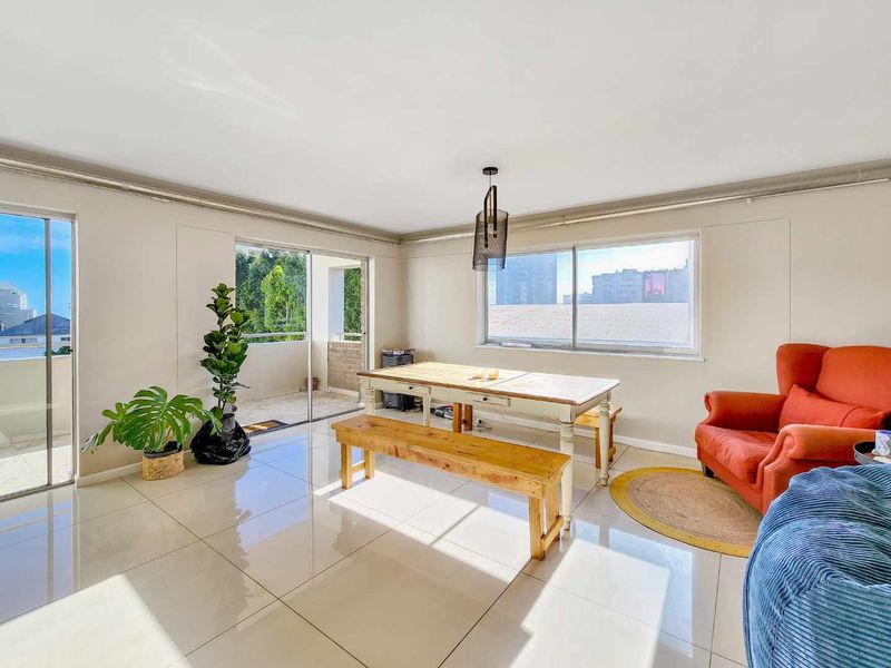 Bright and spacious living area featuring large windows, sliding glass doors leading to a balcony, and polished tiled flooring throughout.