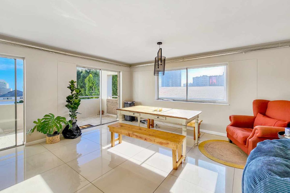 Bright and spacious living area featuring large windows, sliding glass doors leading to a balcony, and polished tiled flooring throughout.