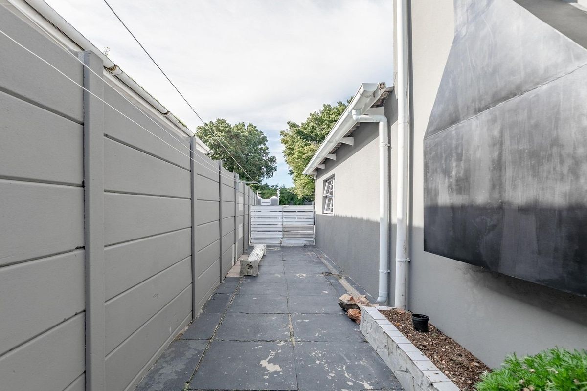 A narrow side passage featuring paved flooring, a boundary wall, and an external metal chimney flue attached to the main building structure.