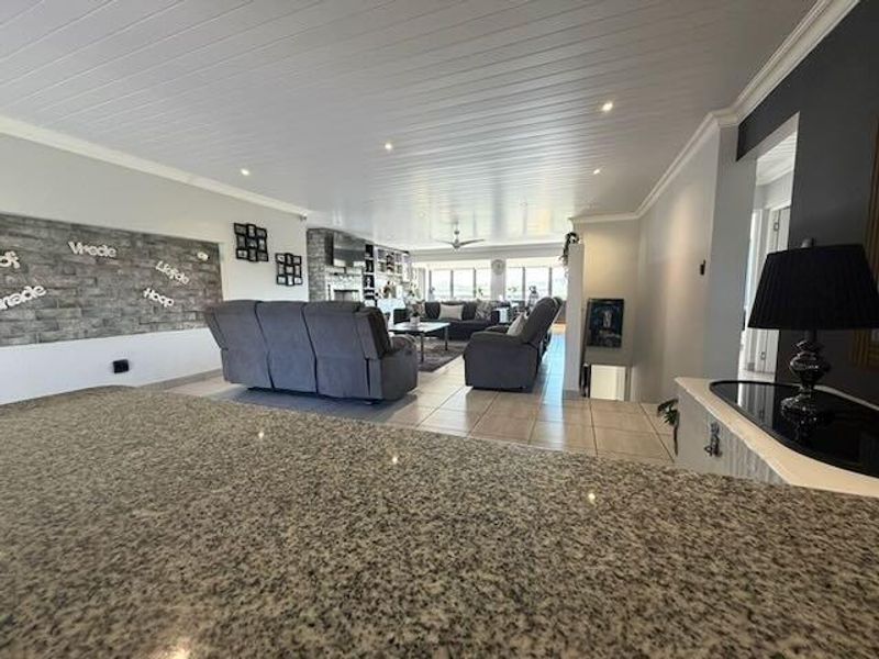 Spacious open-plan living area featuring a granite kitchen island, stone feature wall, and modern tongue and groove ceiling with recessed lighting.