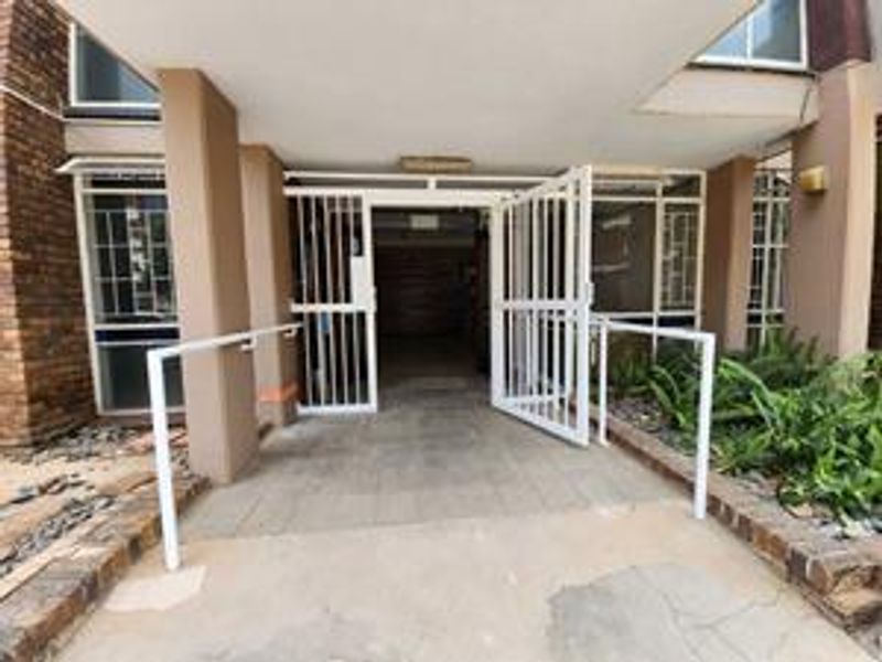 The apartment building entrance features a paved walkway, security gate, and handrails, providing access to the main building lobby.