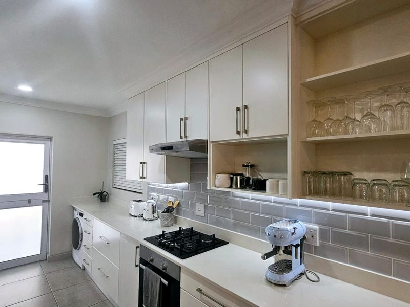 Modern kitchen featuring white cabinetry, quartz countertops, subway tile backsplash, gas hob, built-in oven, and integrated laundry space with direct exterior access.