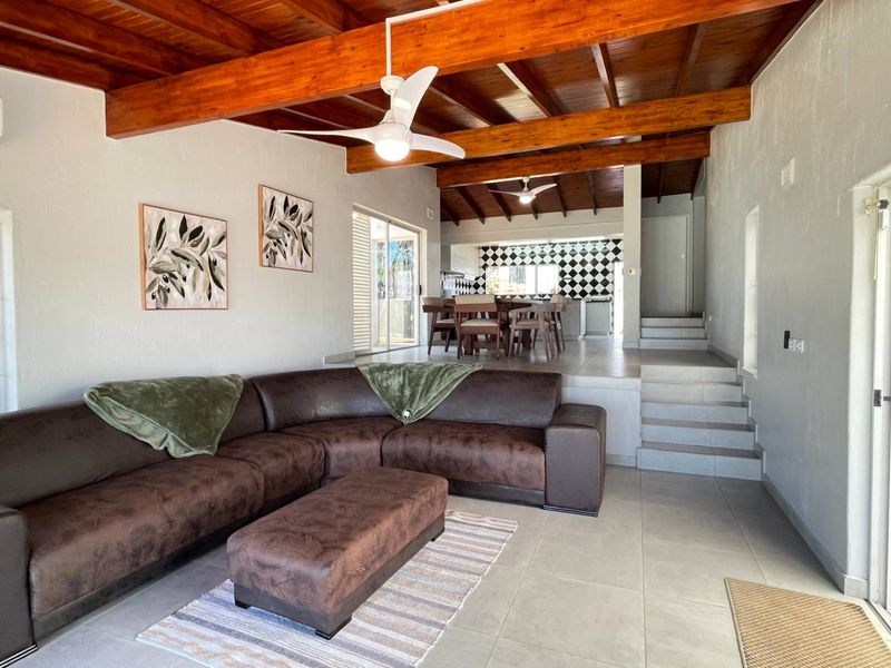 Spacious open-plan living and dining area featuring exposed timber ceiling beams, tiled flooring, and split-system air conditioning, with direct access to outdoor spaces.