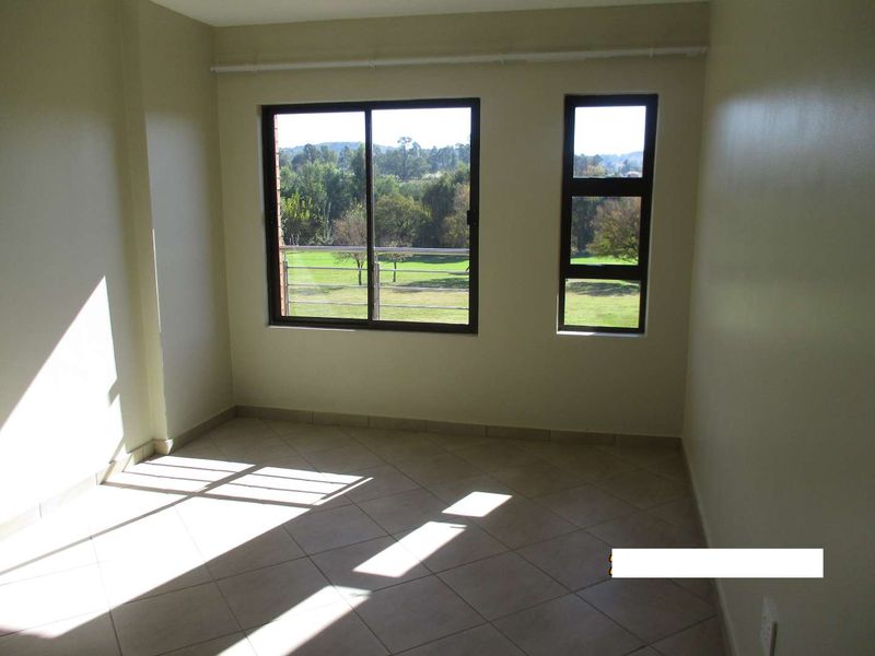 An empty bedroom featuring tiled flooring, neutral walls, and large windows providing natural light and scenic outdoor views.