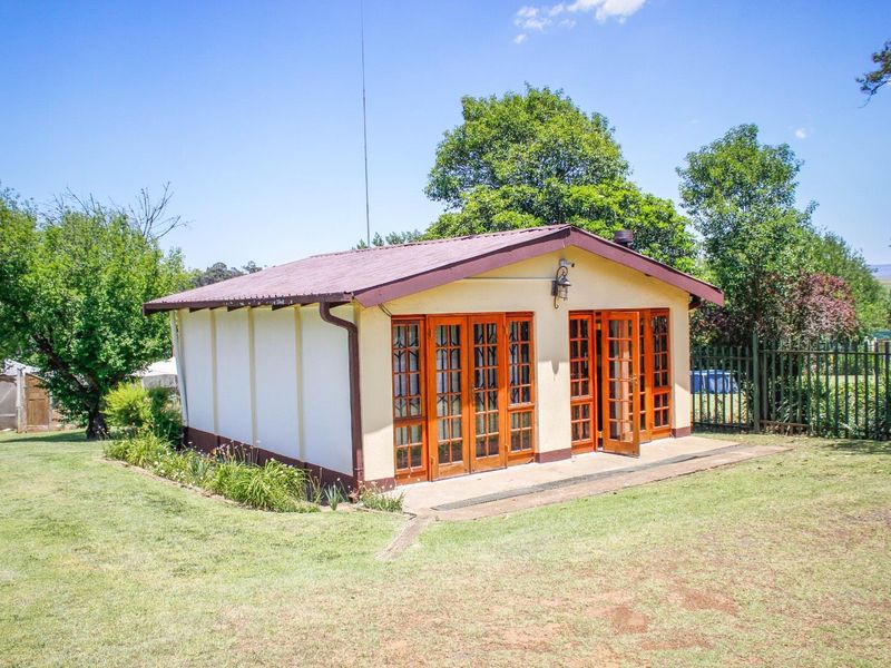 A detached garden structure featuring a metal roof and multiple timber-framed glass doors opening onto a surrounding lawn area.