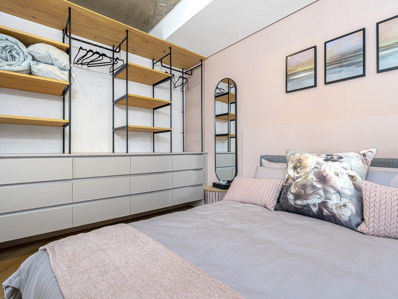 A modern bedroom featuring an exposed concrete ceiling, built-in open shelving, and integrated cabinetry, creating a contemporary and functional living space.