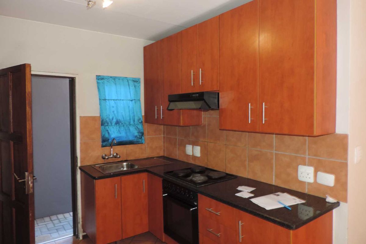A functional kitchen featuring wood-finish cabinetry, a dark granite countertop, a built-in oven with hob, and an extractor fan.