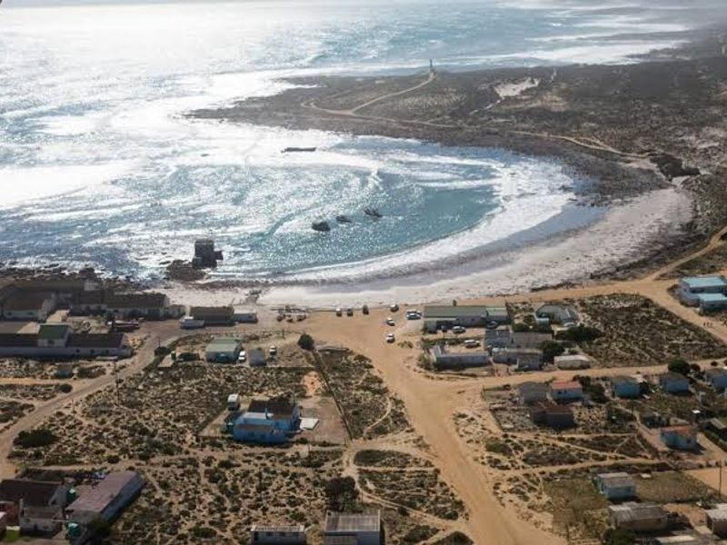 Aerial view of a coastal residential area featuring unpaved roads, scattered dwellings, and direct access to the beach and ocean.