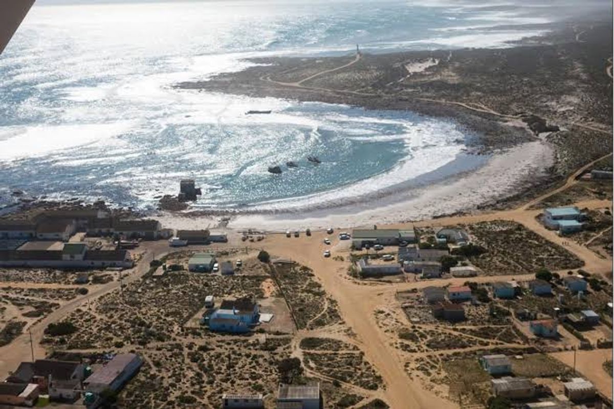Aerial view of a coastal residential area featuring unpaved roads, scattered dwellings, and direct access to the beach and ocean.