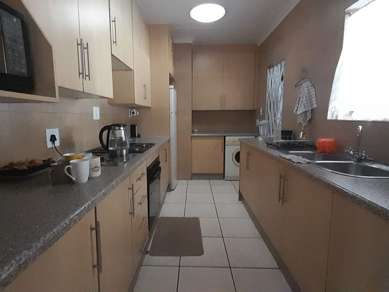 A functional galley-style kitchen featuring laminate cabinetry, laminate countertops, built-in oven, hob, and tiled flooring.