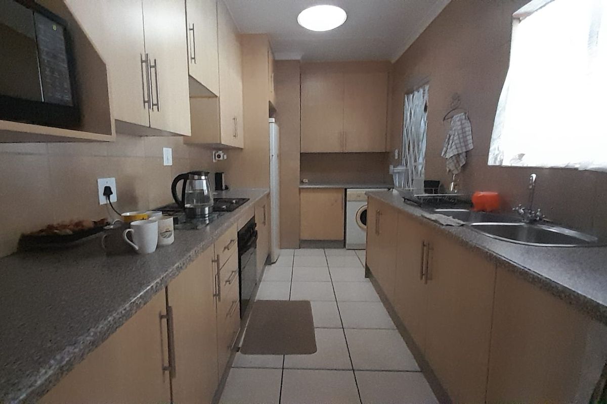 A functional galley-style kitchen featuring laminate cabinetry, laminate countertops, built-in oven, hob, and tiled flooring.