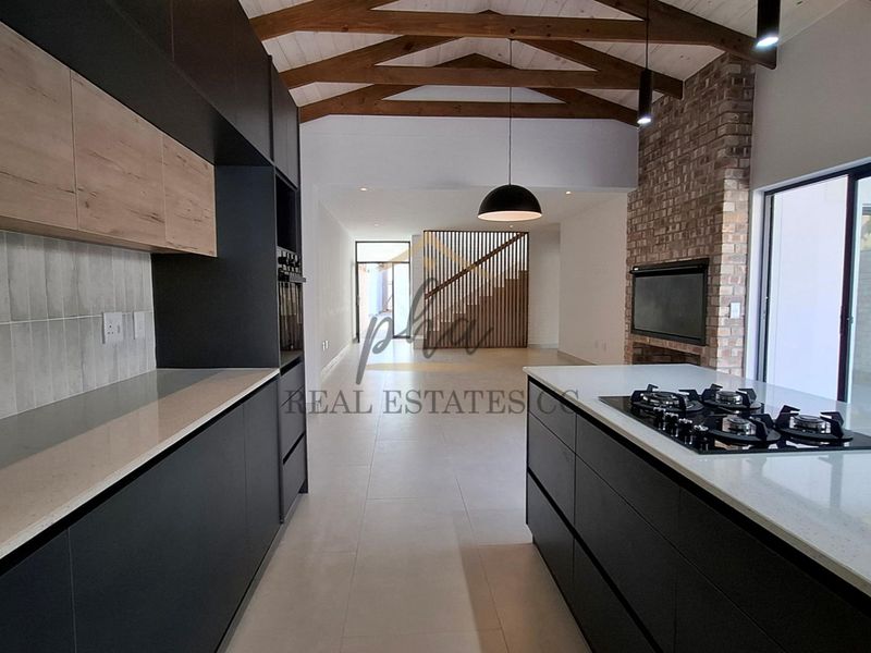 Modern open-plan kitchen and living area featuring exposed timber beams, a brick fireplace, and a sleek kitchen island with a gas hob.