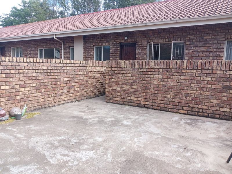 A private rear courtyard featuring a concrete patio area enclosed by face brick boundary walls, attached to a single-story apartment with a tiled roof.