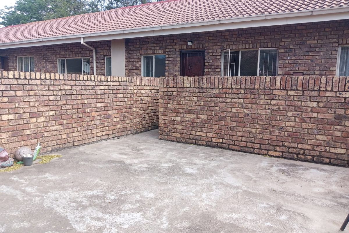 A private rear courtyard featuring a concrete patio area enclosed by face brick boundary walls, attached to a single-story apartment with a tiled roof.