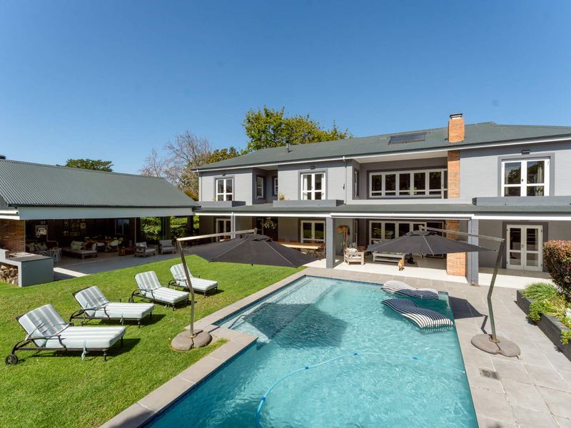Spacious rear garden featuring a swimming pool, paved surround, covered patio area with built-in braai, and a well-maintained lawn.