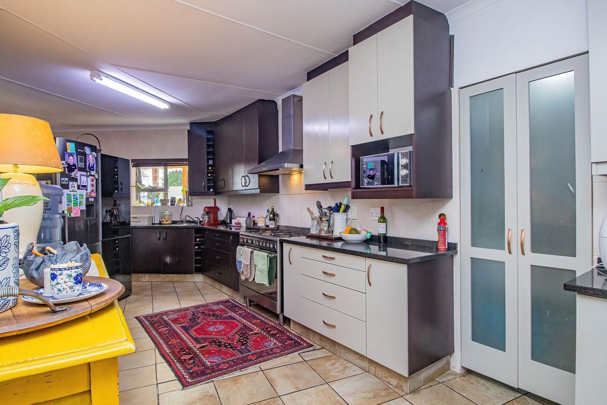A functional kitchen featuring two-tone cabinetry, granite countertops, a stainless steel gas stove with extractor, and tiled flooring with a pantry storage area.
