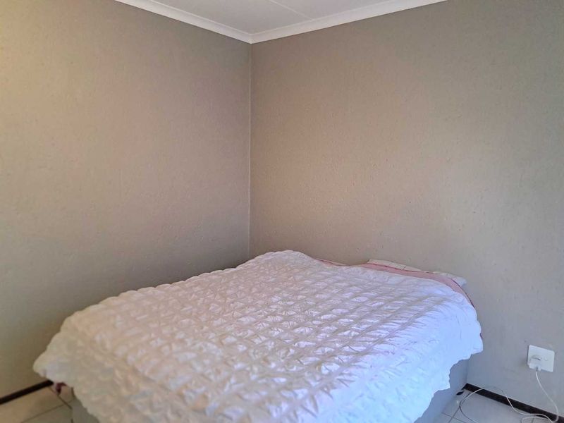 A simple bedroom featuring neutral wall paint, cove cornicing, and tiled flooring.