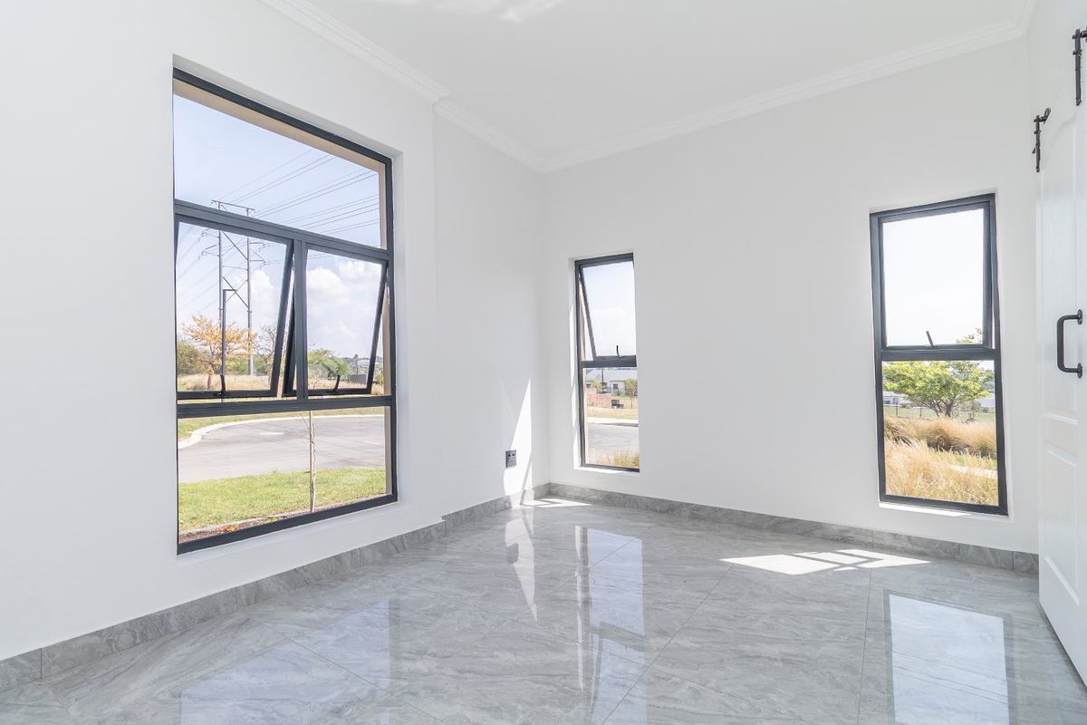 A bright, empty bedroom featuring modern grey porcelain tile flooring, large aluminium-framed windows, and a sliding barn door.