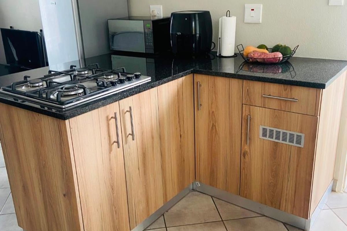 Compact kitchen corner featuring wood-look cabinetry, granite countertops, and a built-in gas hob with ceramic tiled flooring.