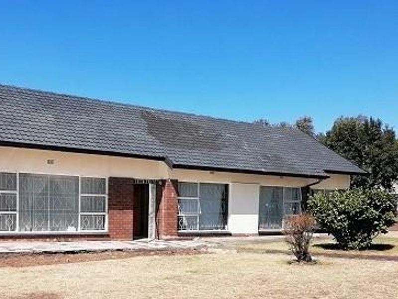 Front exterior view of a single-story brick house featuring a tiled roof, chimney, and security-barred windows with an adjacent concrete patio area.