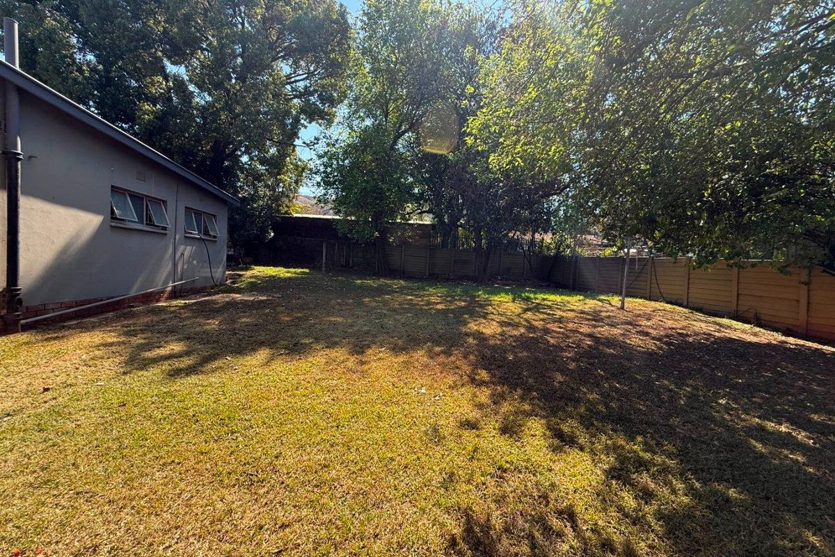 A spacious rear garden featuring a lawn area, mature trees, and a precast concrete boundary wall, adjacent to the side of the house.