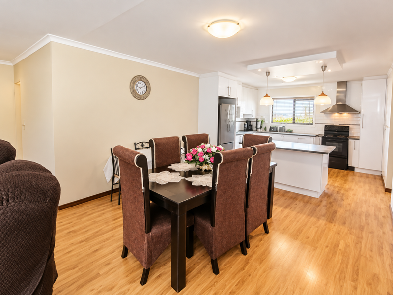 Open-plan kitchen and dining area featuring modern white cabinetry, a central island, laminate flooring, and a subway tile backsplash.