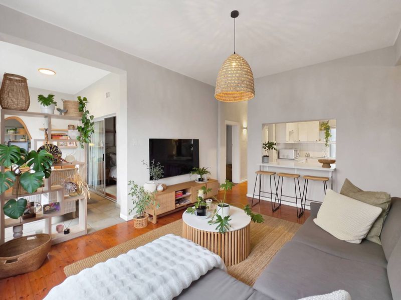 A bright living room featuring polished hardwood floors, a breakfast bar pass-through to the kitchen, and a neutral color palette.