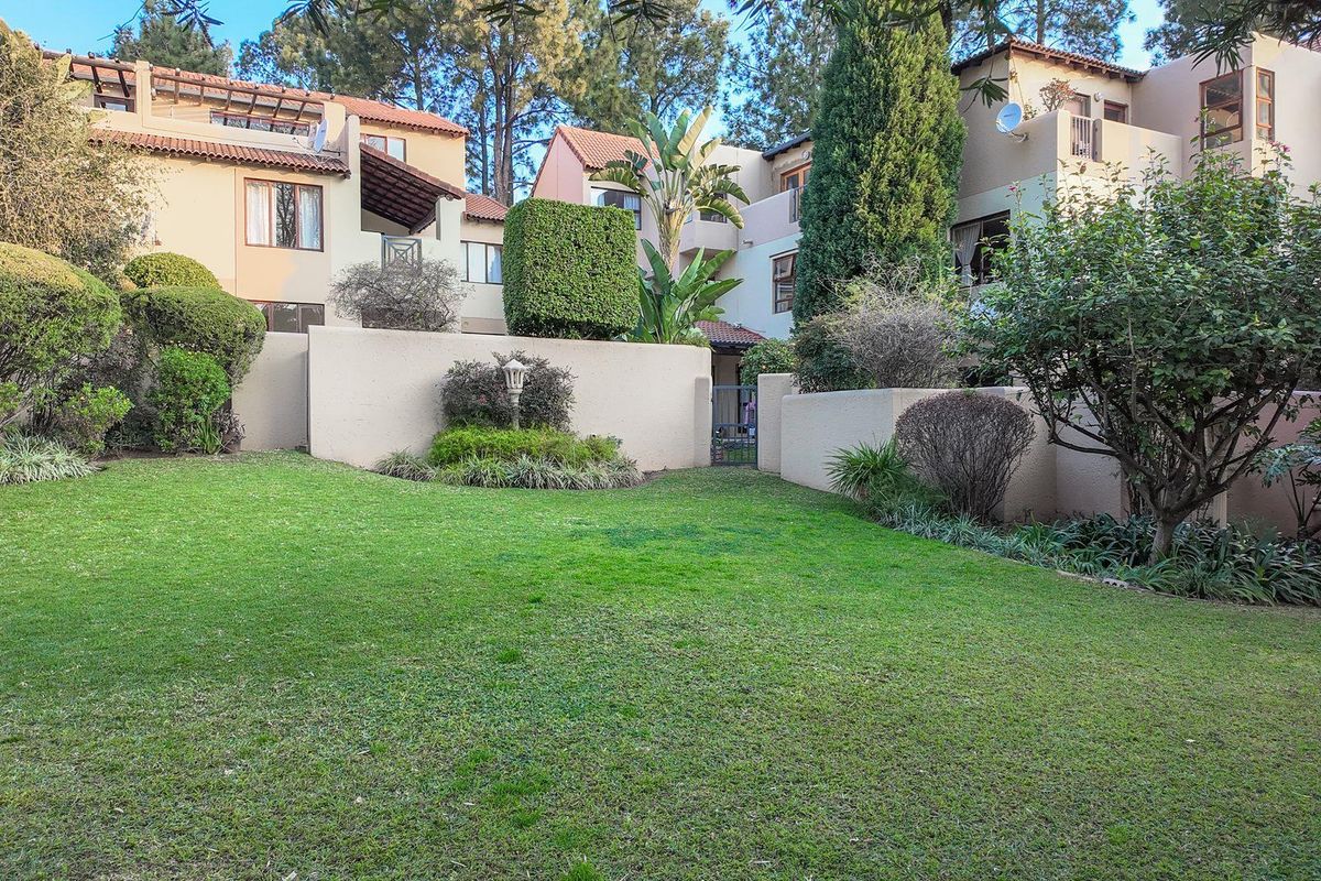 A well-maintained communal garden area featuring manicured lawns and established landscaping, set against the rear facade of a multi-story apartment complex.