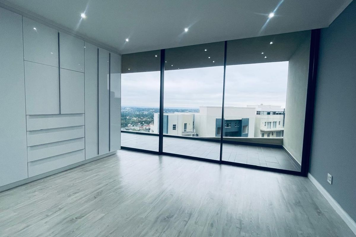 Modern bedroom featuring floor-to-ceiling built-in cabinetry, light wood-look flooring, recessed downlighting, and expansive sliding glass doors opening to a private balcony with city views.