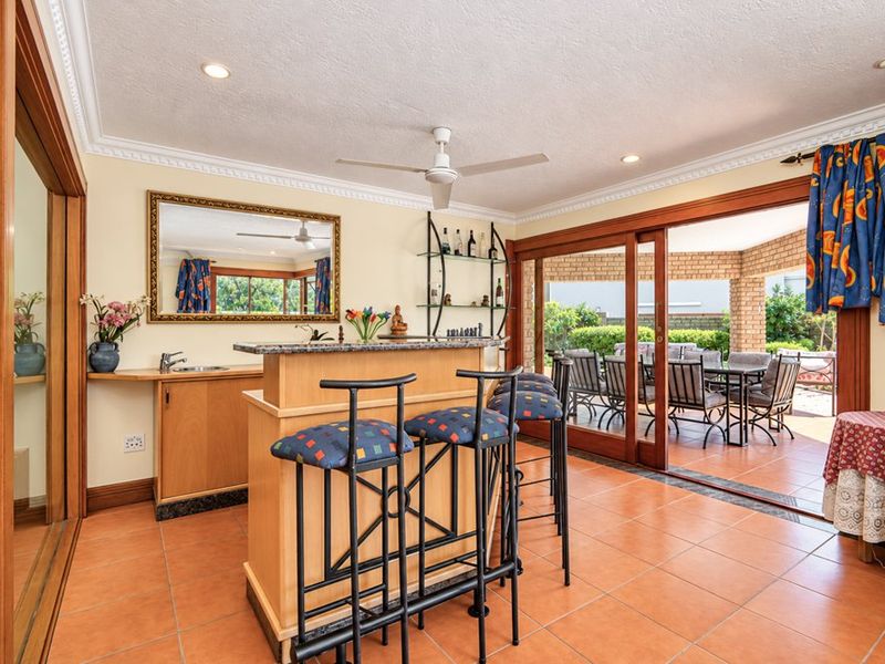 A dedicated bar area featuring a built-in counter with sink, tiled flooring, and seamless access to the outdoor patio through large sliding glass doors.