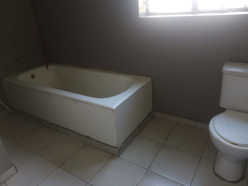 A basic bathroom featuring a built-in bathtub and toilet with tiled flooring, requiring cosmetic updates to improve its overall condition and appeal.