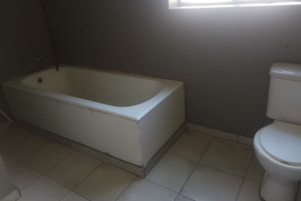 A basic bathroom featuring a built-in bathtub and toilet with tiled flooring, requiring cosmetic updates to improve its overall condition and appeal.