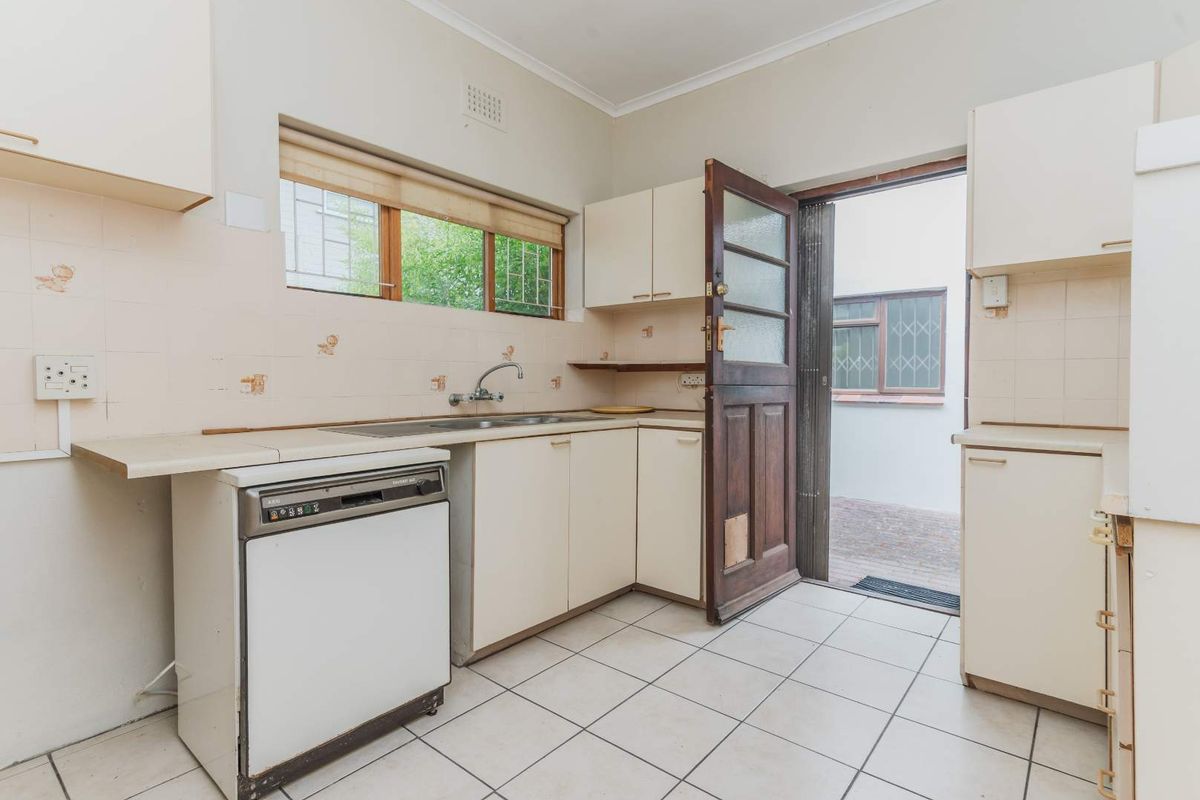 A dated kitchen featuring tiled flooring, built-in cabinetry, a stainless steel sink, and direct access to an outdoor area.