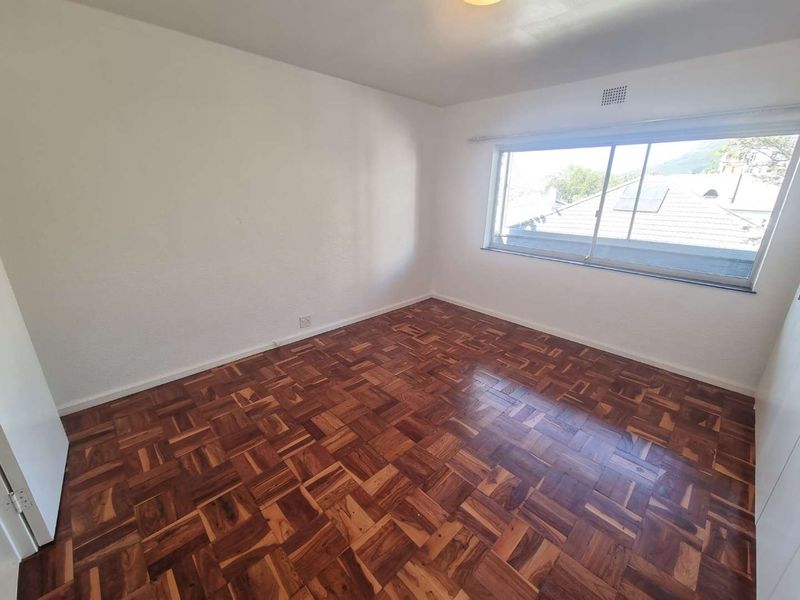 A bright, empty bedroom featuring classic parquet timber flooring and a large sliding window with natural light.